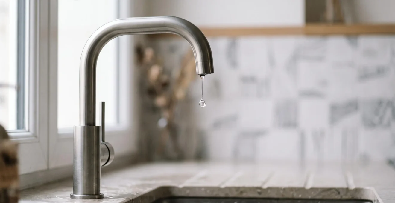 Robinet moderne en gros plan avec une goutte d'eau suspendue, symbolisant l'équilibre entre économie et confort dans une salle de bain française